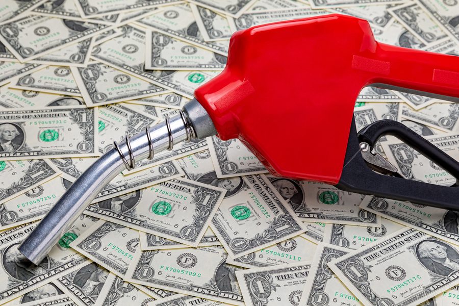 Gas pump nozzle lying on a pile of dollar bills